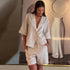 Woman wearing a beige linen outfit standing in a room with decorative elements.
